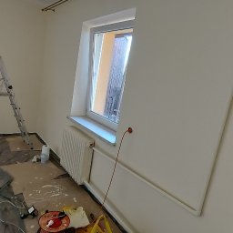 Marek Rząsa - Pokój po malowaniu na biało, z zabezpieczoną podłogą i grzejnikiem. Widoczna drabina malarska i akcesoria malarskie. Świeżo pomalowane ściany.