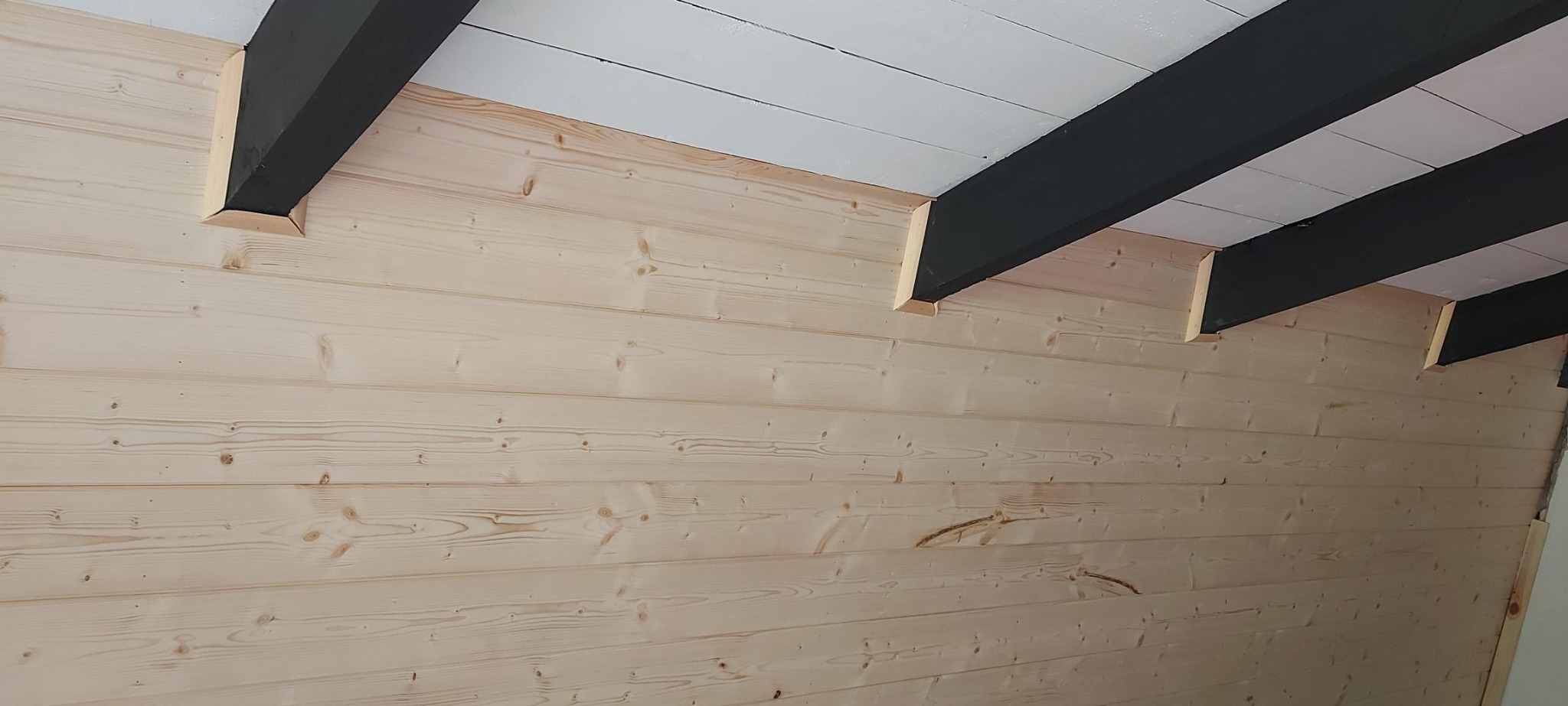 Ściana i sufit wykończone boazerią, pomalowane belki stropowe na czarno, sufit na biało. Widok z dołu, ukazujący detale wykończenia.