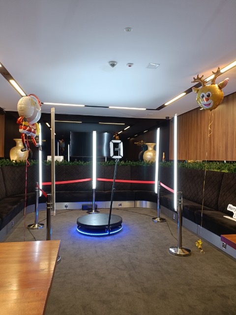 Fotobudka 360 z oświetleniem LED i świątecznymi dekoracjami (balony renifer i Mikołaj) ustawiona w eleganckim wnętrzu z sofami i dekoracyjnymi wazami.