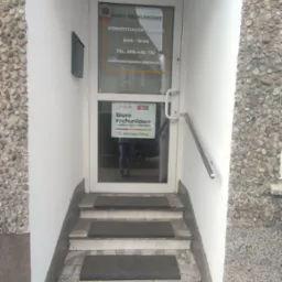 Wejście do biura rachunkowego z godzinami otwarcia na szybie i informacją o współpracy z mBankiem. Schody z wycieraczkami prowadzą do drzwi.