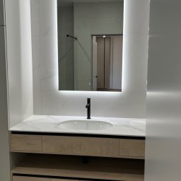 ANDRII KOLTSOV STREAMCO MEBLE - Nowoczesna łazienka z podświetlanym lustrem i szafką z drewnianymi frontami. Widoczna armatura w kolorze czarnym i marmurowy blat. Minimalistyczny design.