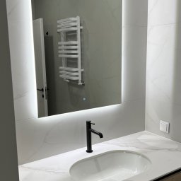 ANDRII KOLTSOV STREAMCO MEBLE - Nowoczesna łazienka z umywalką wpuszczaną w marmurowy blat, podświetlane lustro i grzejnik drabinkowy. Minimalistyczny design, jasne kolory.