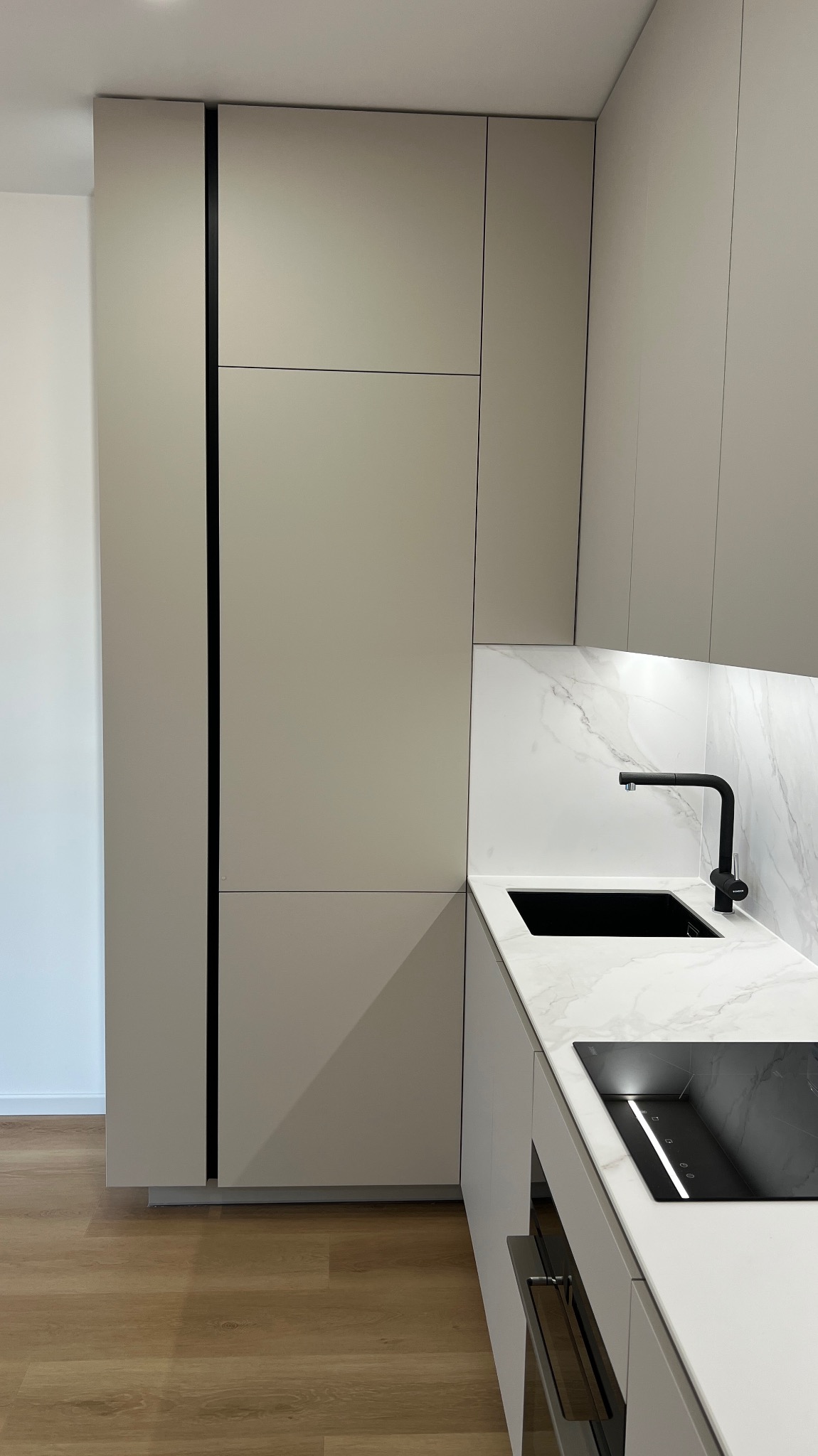 Nowoczesna kuchnia z beżowymi szafkami, czarną armaturą i blatem z imitacją marmuru. Minimalistyczny design, oświetlenie LED pod szafkami.