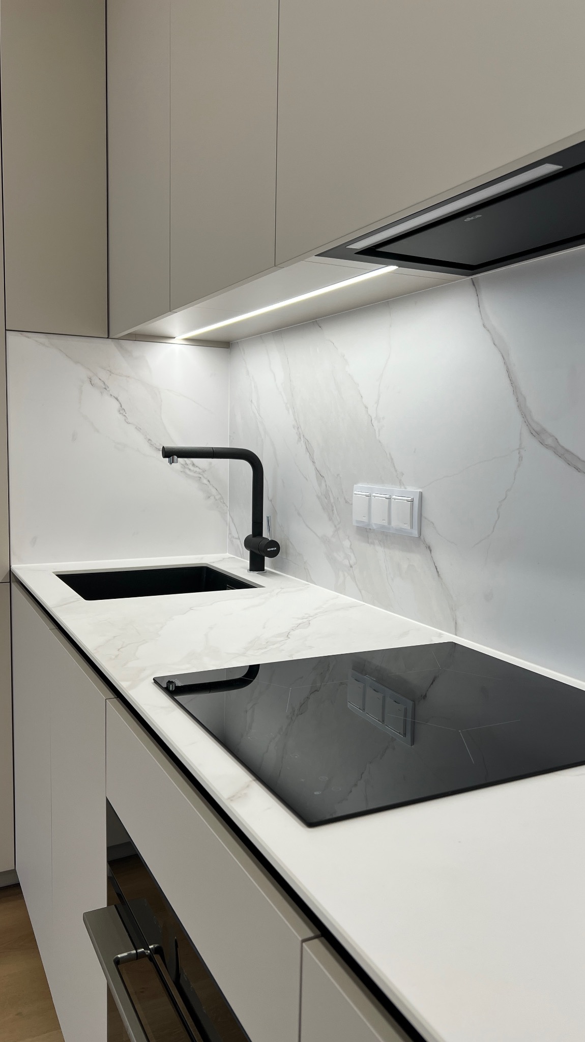 Nowoczesna kuchnia: biały blat z marmurowym wzorem, czarny zlew i płyta indukcyjna. Minimalistyczne szafki i oświetlenie LED podkreślają elegancję.