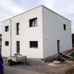 RAFA - Nowoczesny, dwukondygnacyjny dom z białą elewacją, czarnymi oknami i przyczepką na posesji w trakcie prac wykończeniowych.