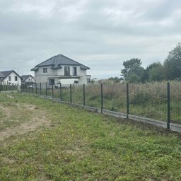 Marta Koceja - Nowoczesne ogrodzenie panelowe z podmurówką betonową na tle budynków mieszkalnych i zachmurzonego nieba. Widok na posesję z zewnątrz.