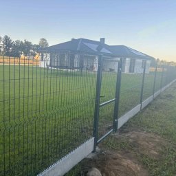 Marta Koceja - Nowoczesne ogrodzenie panelowe z bramką wejściową, osadzone na betonowej podmurówce, otaczające trawnik przed domem z panelami solarnymi na dachu.