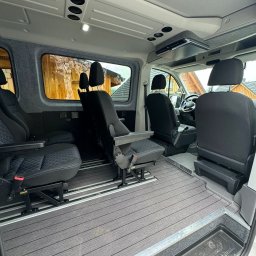 Świerkowe Chatki w Koniakowie - Przestronne wnętrze busa z regulowanymi fotelami na szynach, wykończone szarą wykładziną imitującą drewno i jasną tapicerką. Widok z tyłu kabiny pasażerskiej.