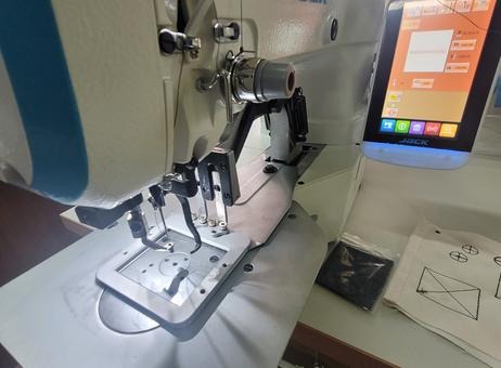 Detale automatycznej maszyny szwalniczej Jack z panelem dotykowym, widoczne elementy mechaniczne i wzór szycia na tkaninie. Precyzyjne wykonanie.