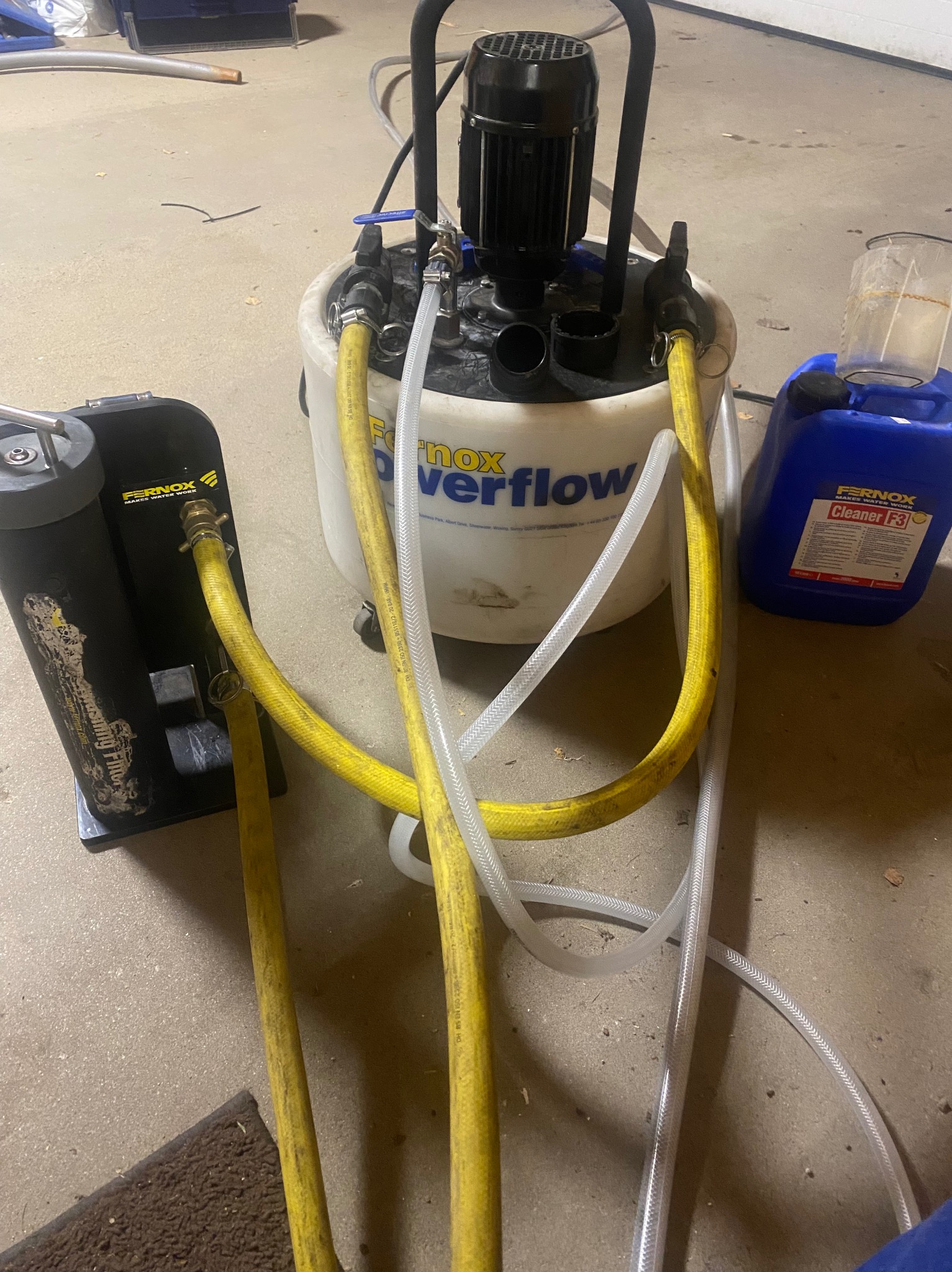 Urządzenie Fernox Overflow do płukania instalacji grzewczych z żółtymi i przezroczystymi wężami oraz pojemnikiem z płynem czyszczącym Fernox F3.