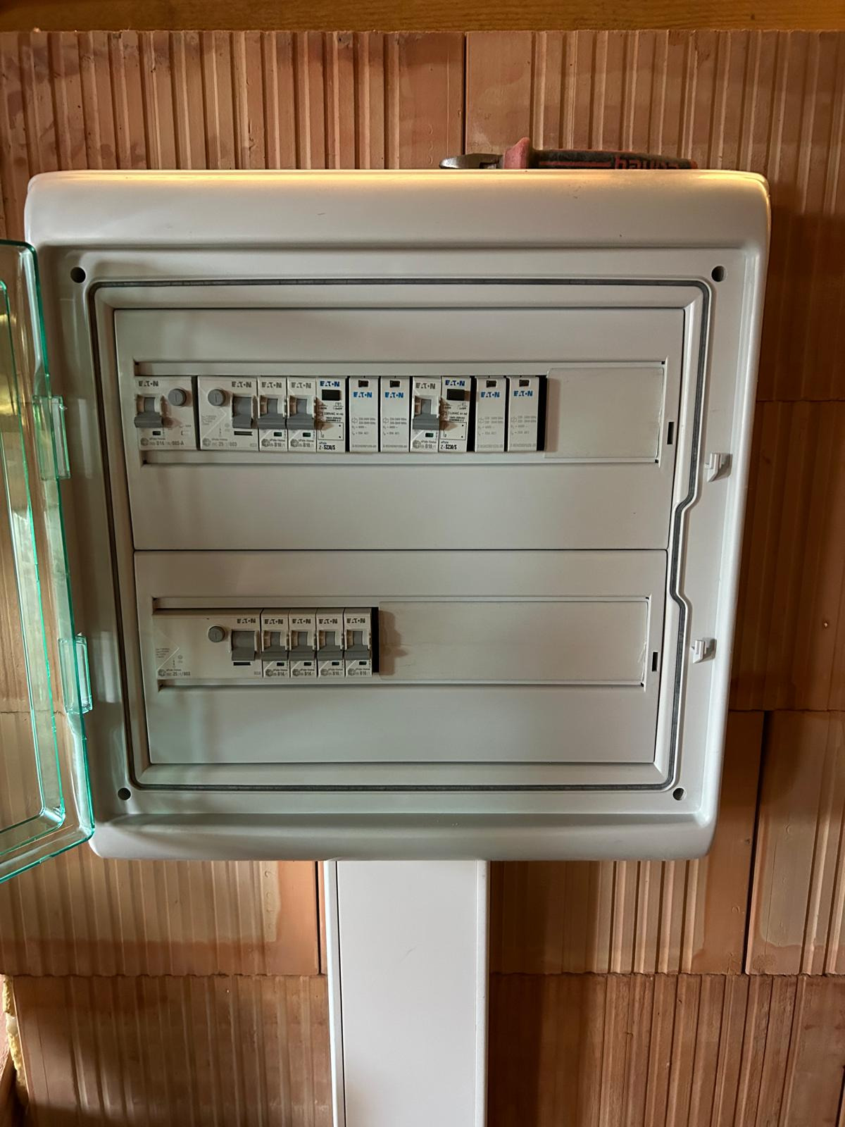 Rozdzielnica elektryczna Eaton z otwartą osłoną, zamontowana na ceglanej ścianie. Nad nią leży klucz płaski. Widoczne bezpieczniki i wyłączniki.