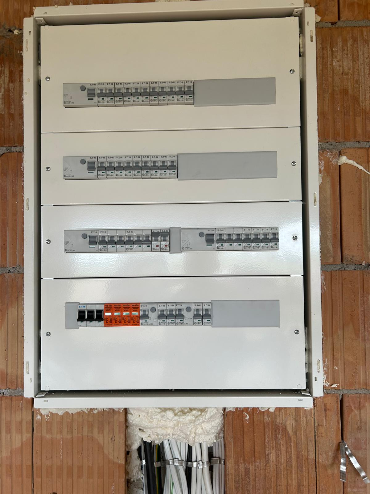 Rozdzielnica elektryczna Eaton w obudowie, zamontowana na ceglanej ścianie, z widocznymi przewodami i zabezpieczeniami. Widok od frontu, oświetlenie naturalne.