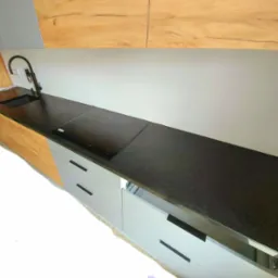 Czarny blat granitowy w kuchni z płytą indukcyjną i minimalistycznym zlewem, satynowe wykończenie, jasne drewniane i szare szafki, nowoczesny design.