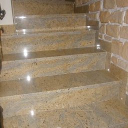 Granmarys S C M.Siuda R.Siuda - Kamienne schody wewnętrzne z beżowego granitu, dopasowane do kamiennej ściany, z delikatnym oświetleniem punktowym na krawędziach stopni.