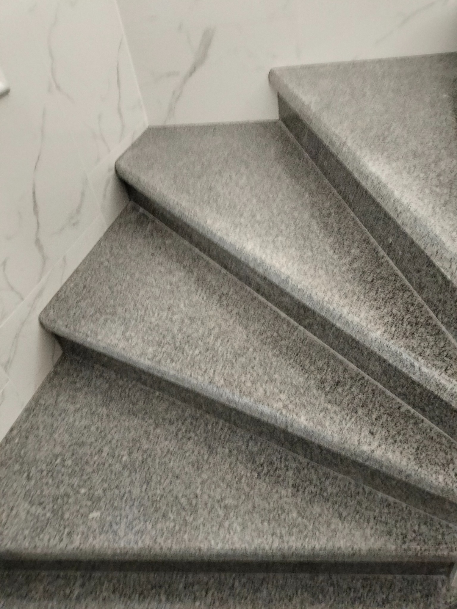 Granitowe schody wewnętrzne z zaokrąglonymi krawędziami, przylegające do marmurowej ściany, prezentują trwałość i elegancję wykończenia.