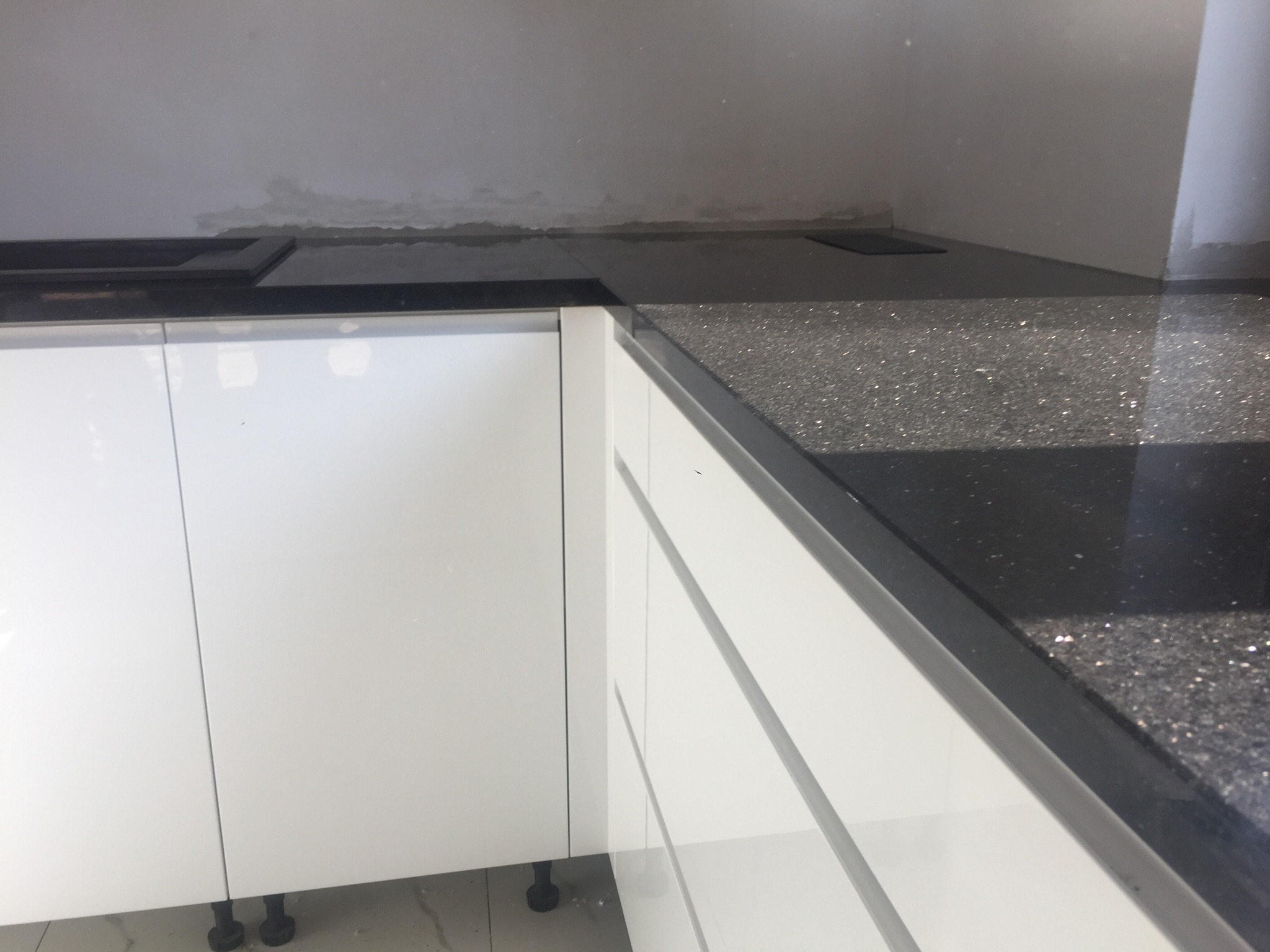 Błyszczący, czarny blat kamienny z brokatowym wzorem, zamontowany na białych szafkach kuchennych. Widoczny fragment zlewu i płyty grzewczej.