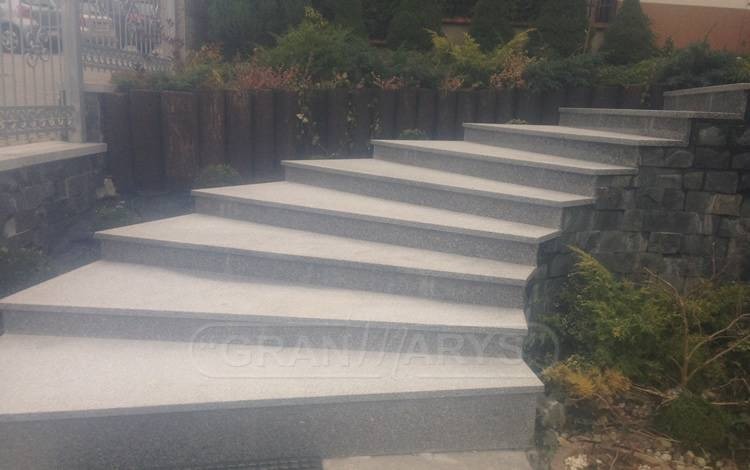 Zewnętrzne schody kamienne z szarego granitu, prowadzące do ogrodu. Widoczne rośliny ozdobne i mur z kamienia naturalnego. Kąt ujęcia z dołu.