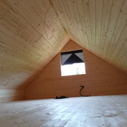 WOOD&HOUSE - Drewniane wnętrze poddasza z oknem w kształcie trójkąta, wykończone jasnymi deskami. Widoczna instalacja elektryczna i czarny materiał zabezpieczający okno.
