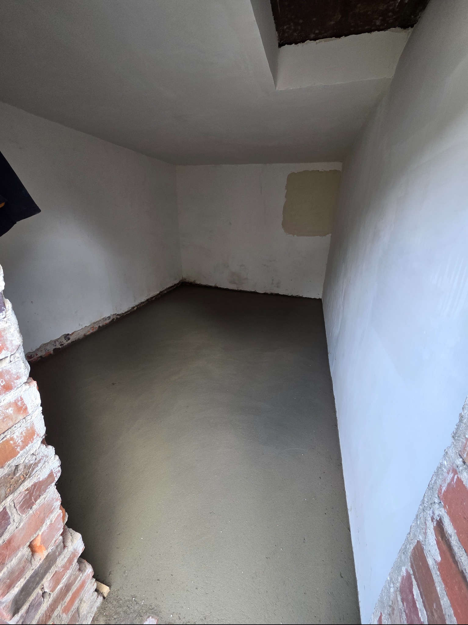 Wnętrze w trakcie wylewki podłogi, ściany przygotowane pod malowanie. Widoczne fragmenty ceglanej konstrukcji. Surowy stan wykończenia.