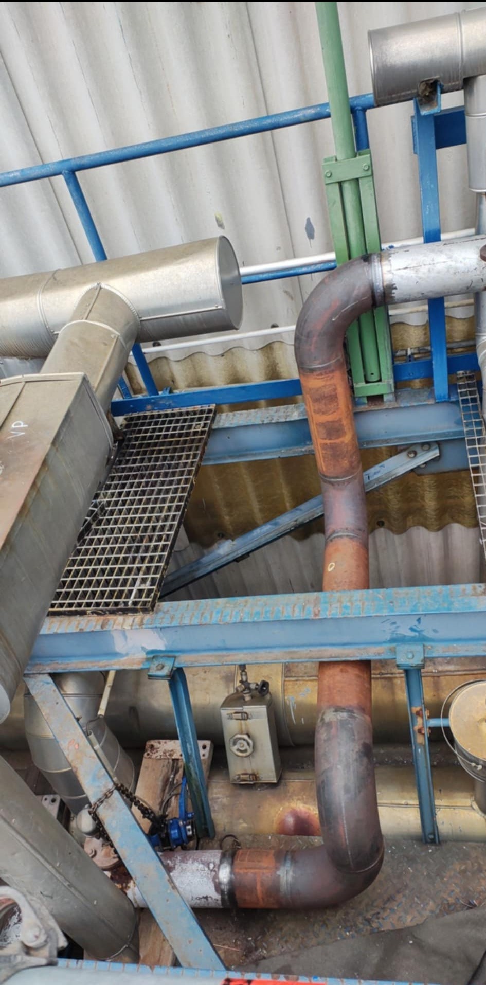 Metalowa konstrukcja z rurami, kratami i elementami instalacji przemysłowej w hali. Widoczne ślady spawania i elementy mocujące.