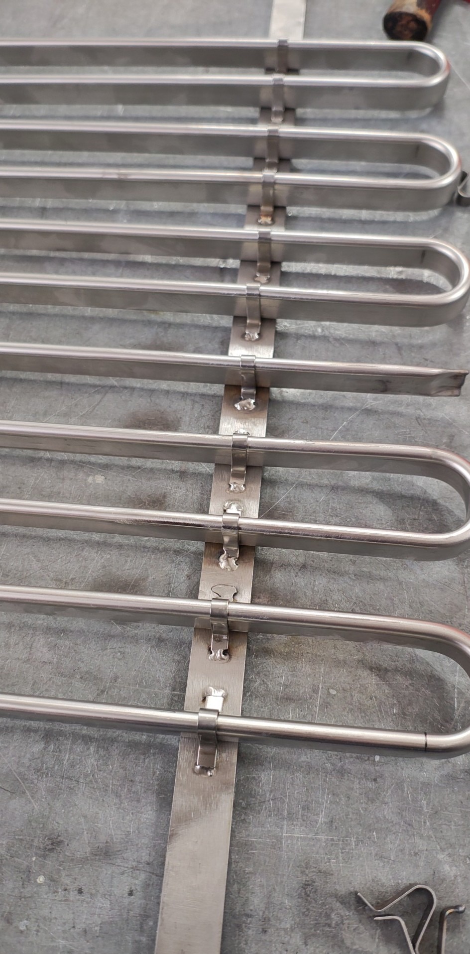 Detal spawanej konstrukcji ze stali nierdzewnej, z widocznymi spawami i elementami mocującymi, na tle metalowej powierzchni roboczej.