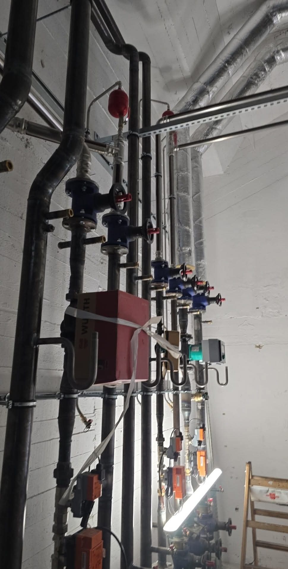 Kompleksowa instalacja centralnego ogrzewania: liczne rury, zawory, czujniki i przewody. Widoczne elementy montażowe i izolacja. Całość w pomieszczeniu technicznym.