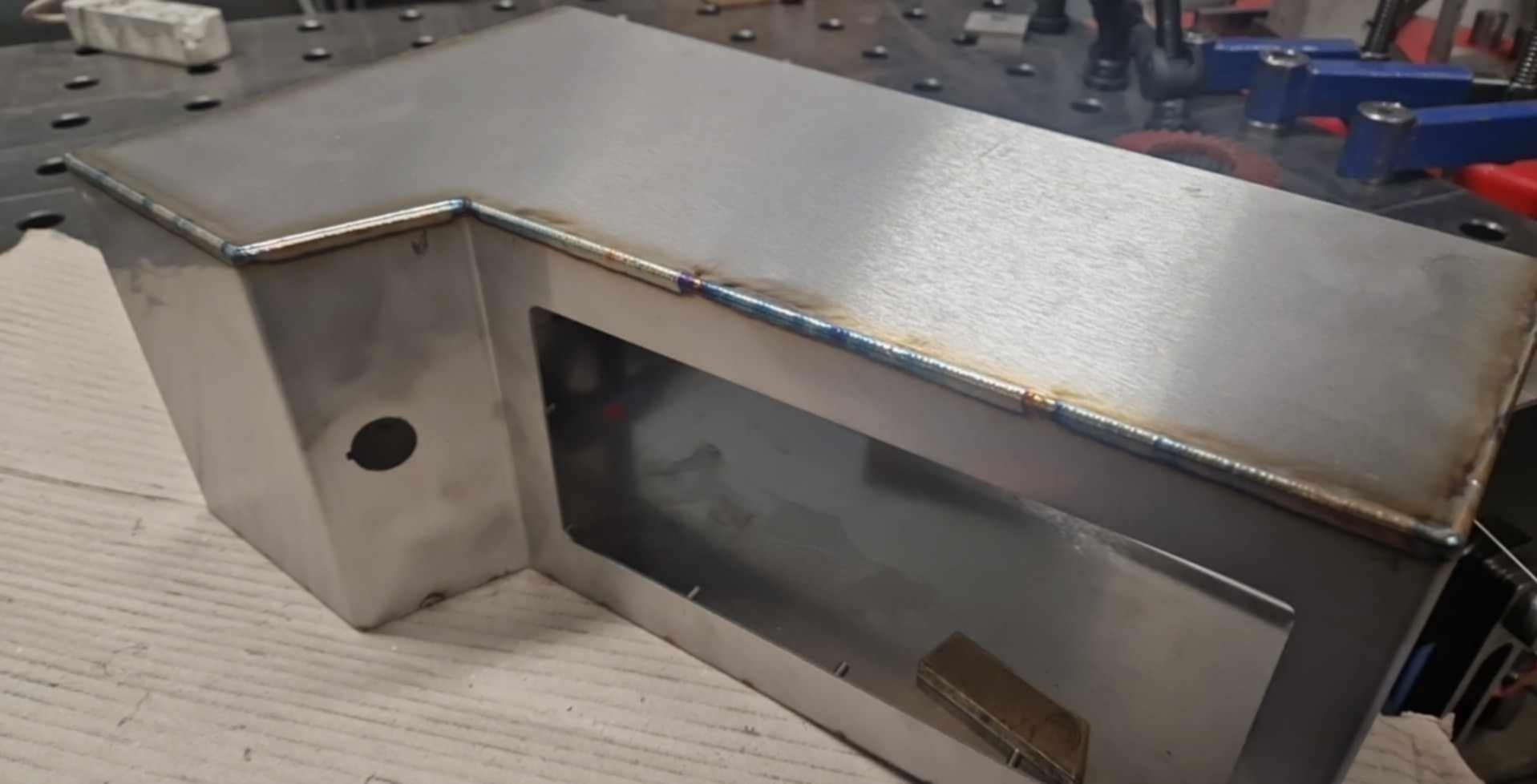 Spawana, metalowa obudowa z otworem i widocznymi spawami, wykonana w Bielawie. Detal konstrukcji ze stali nierdzewnej na stole spawalniczym.