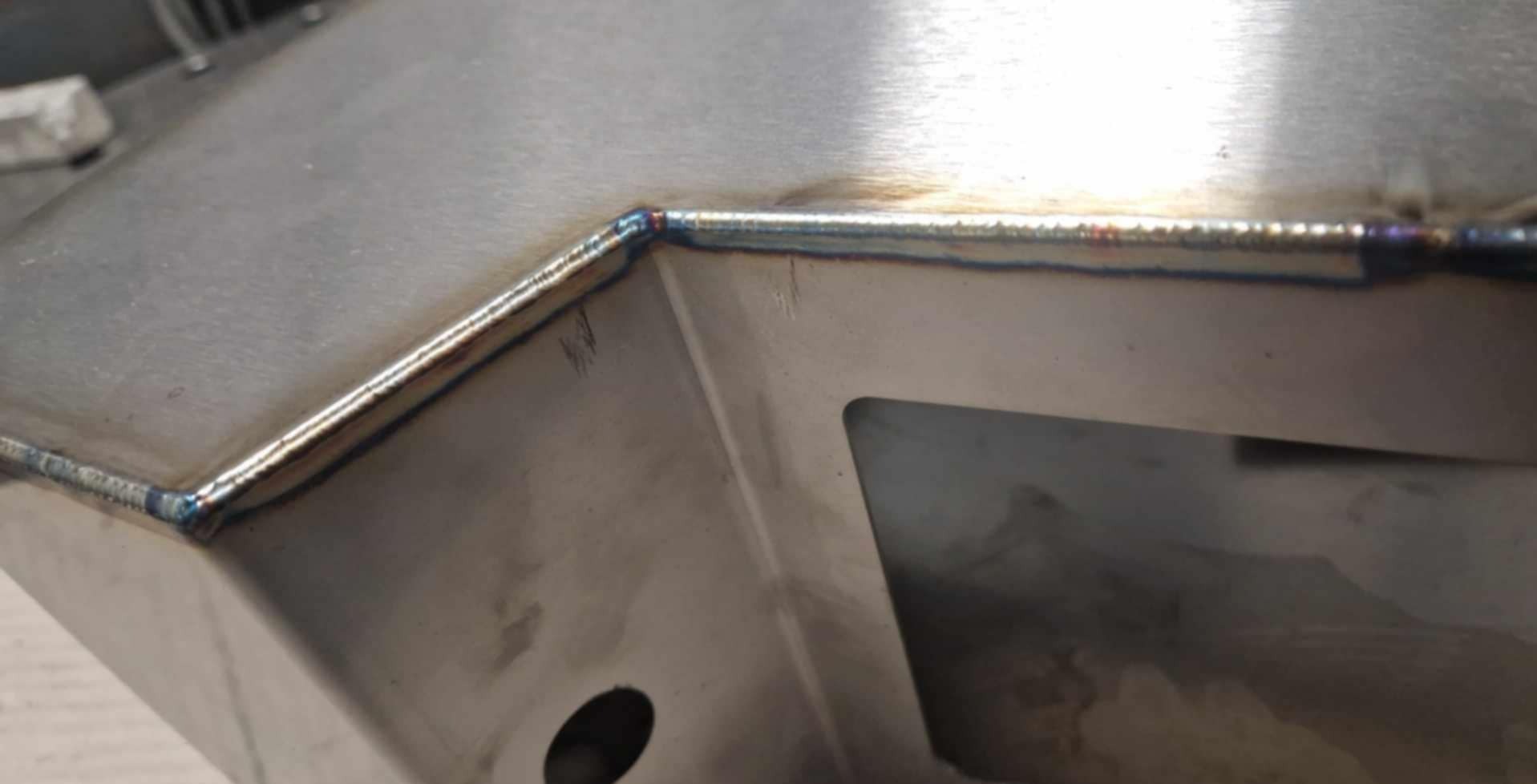 Szlifowane metalowe elementy konstrukcyjne połączone precyzyjnym spoiwem spawalniczym, widoczne detale obróbki i otwory montażowe.