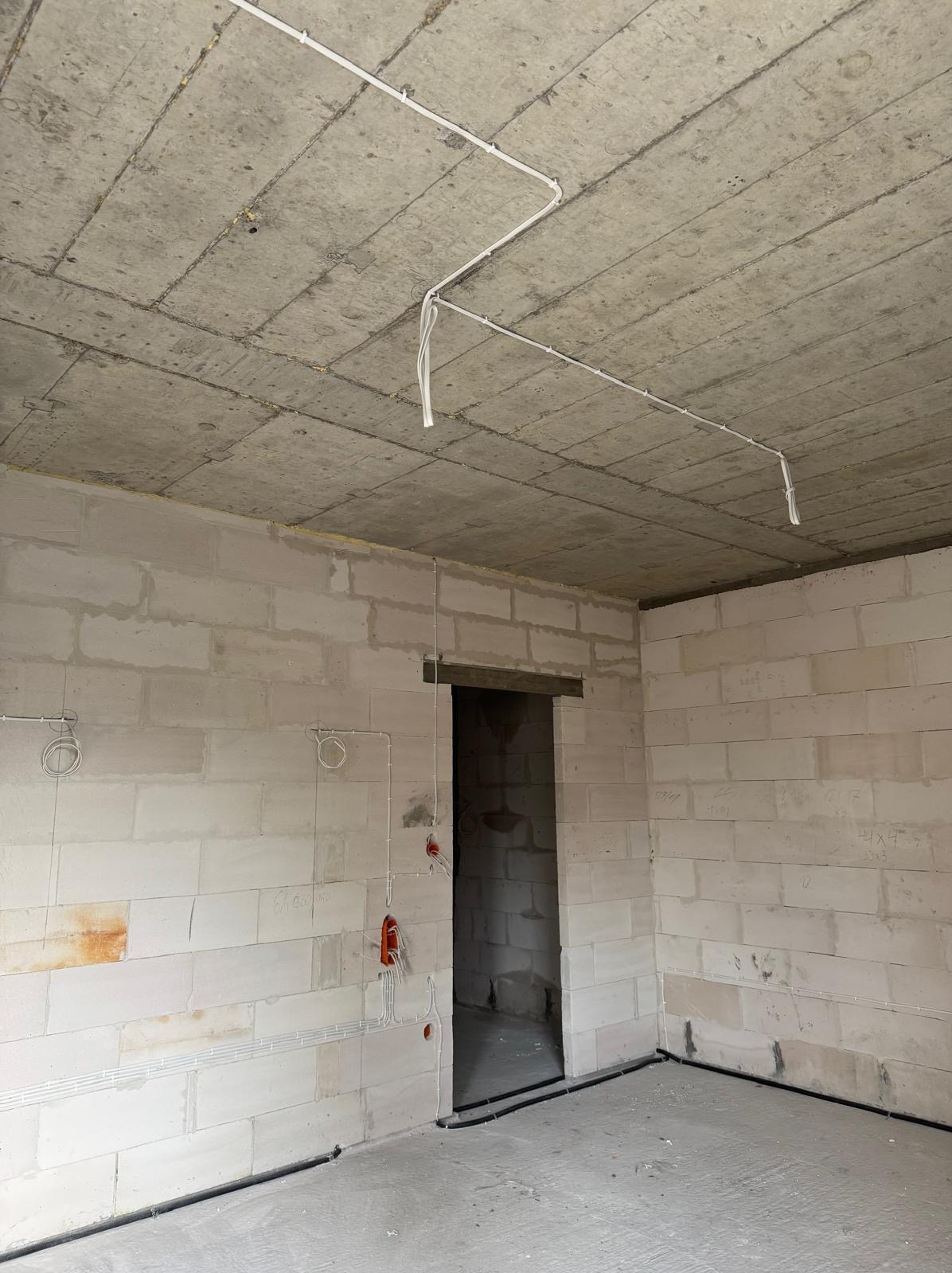 Instalacja elektryczna w surowym wnętrzu z białego bloczka, widoczne przewody na suficie i ścianach. Prace elektryczne w Markuszowie przed tynkowaniem.