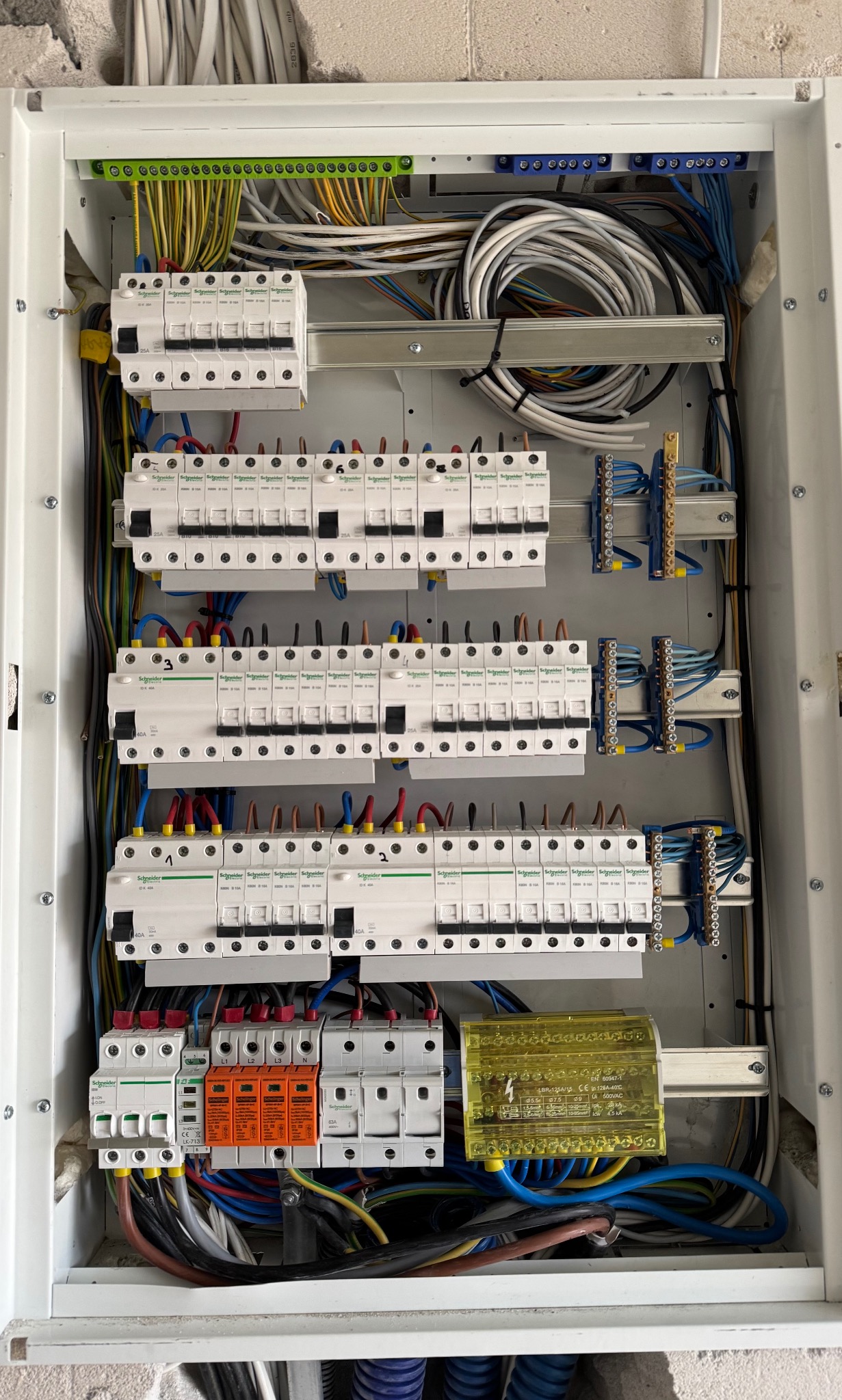 Rozdzielnica elektryczna Schneider z bezpiecznikami, przewodami i listwami zaciskowymi w białej obudowie, widok z bliska, instalacja w trakcie podłączenia.