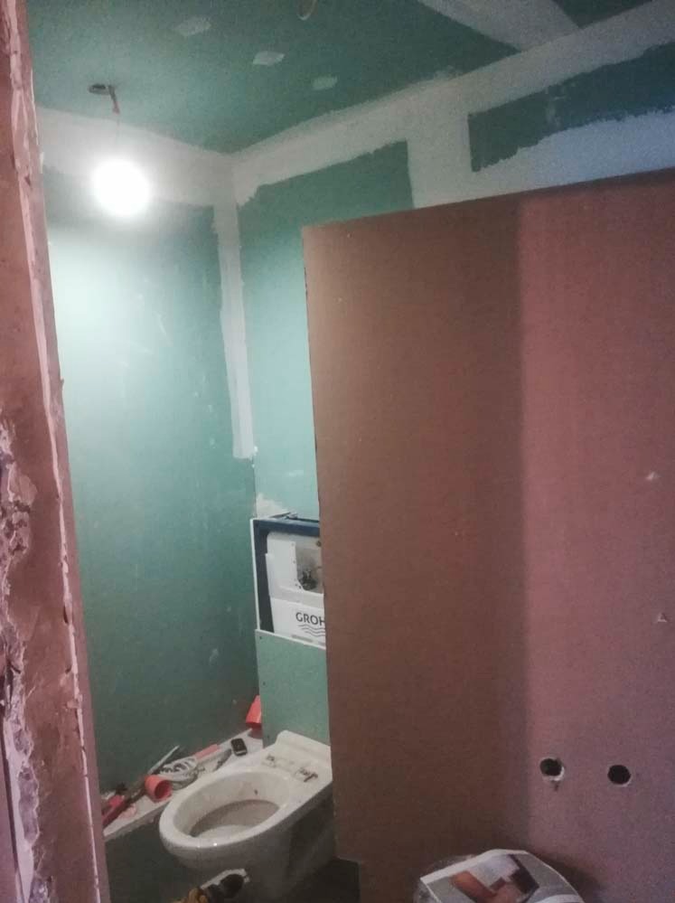 Łazienka w trakcie remontu: ściany z płyt karton-gips, widoczna instalacja toalety podtynkowej Grohe. Prace wykończeniowe w toku, widoczne narzędzia i materiały.