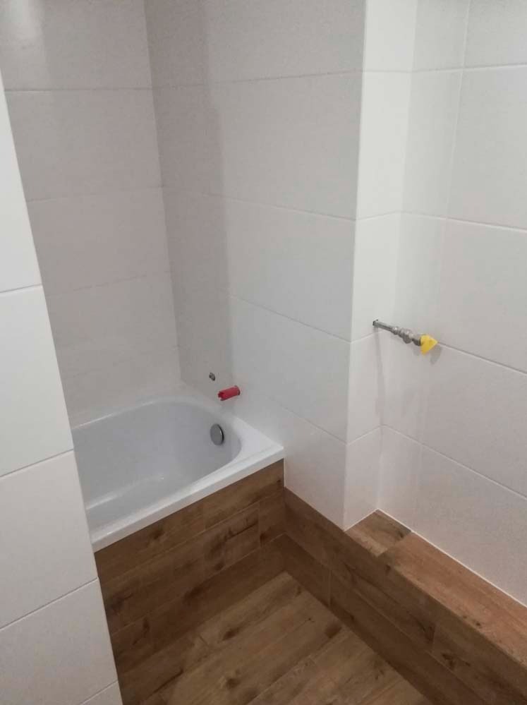 Wykończona łazienka w Sicienko: białe płytki ścienne, obudowa wanny imitująca drewno, armatura. Minimalistyczny design, czystość i funkcjonalność.