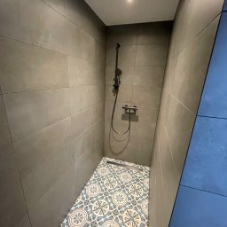 Dominik Dzięgiel - Nowoczesna kabina prysznicowa z szarymi płytkami ściennymi i wzorzystą, niebiesko-białą podłogą. Minimalistyczna armatura i oświetlenie punktowe.