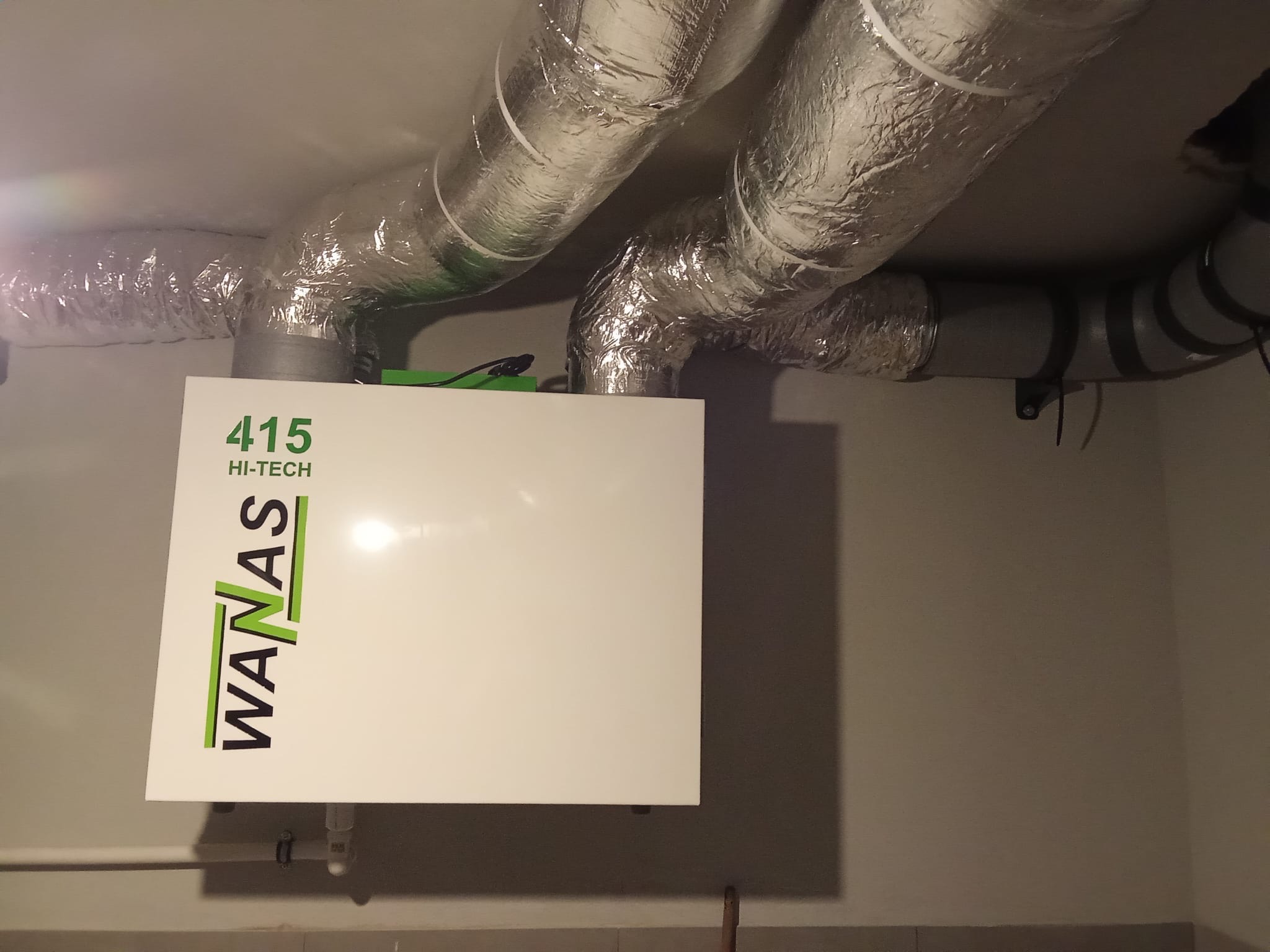 Centrala wentylacyjna WanAs 415 Hi-Tech z izolowanymi przewodami wentylacyjnymi, zamontowana przy suficie w pomieszczeniu o jasnych ścianach.
