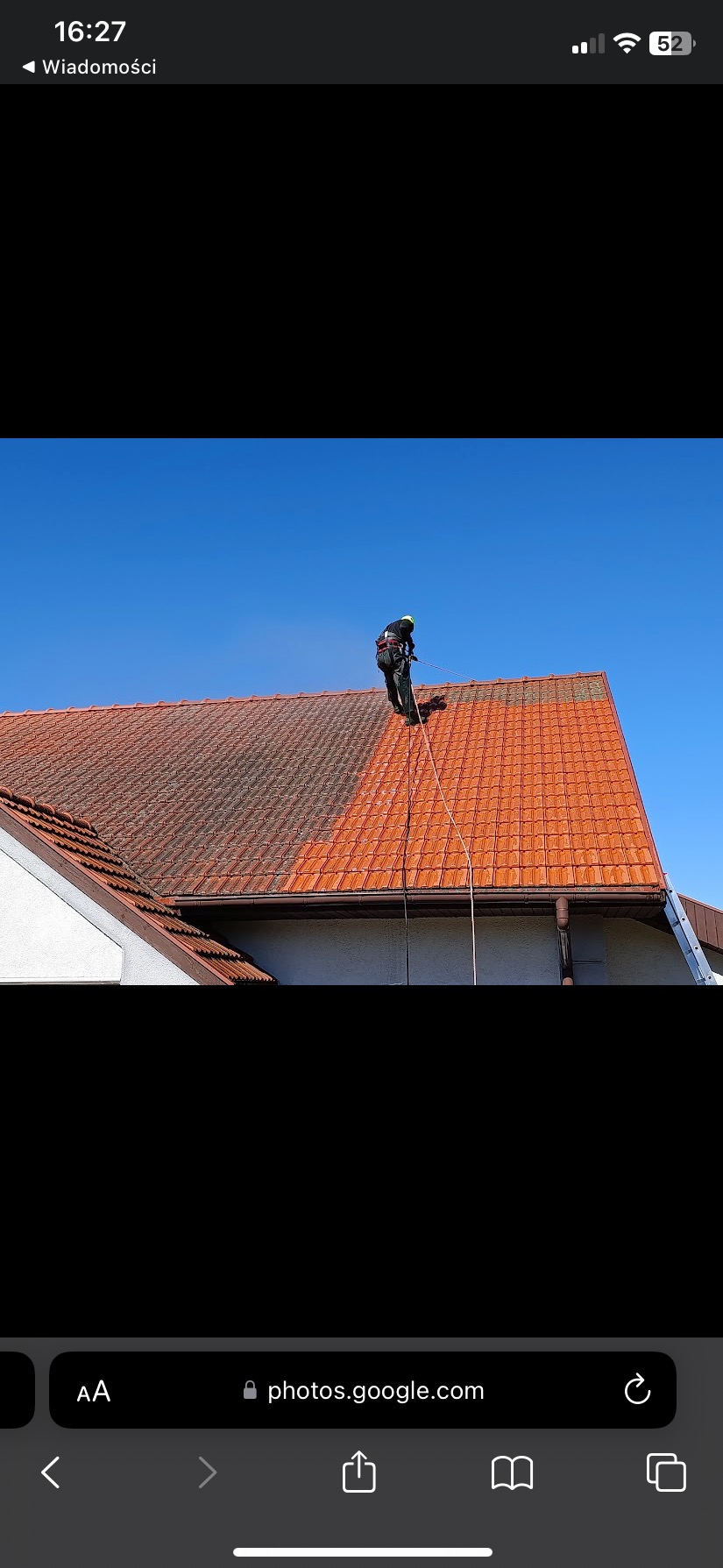 Częściowo wyczyszczony dach z czerwonej dachówki. Widoczna różnica między czystą a zabrudzoną powierzchnią. Pracownik w uprzęży na dachu.