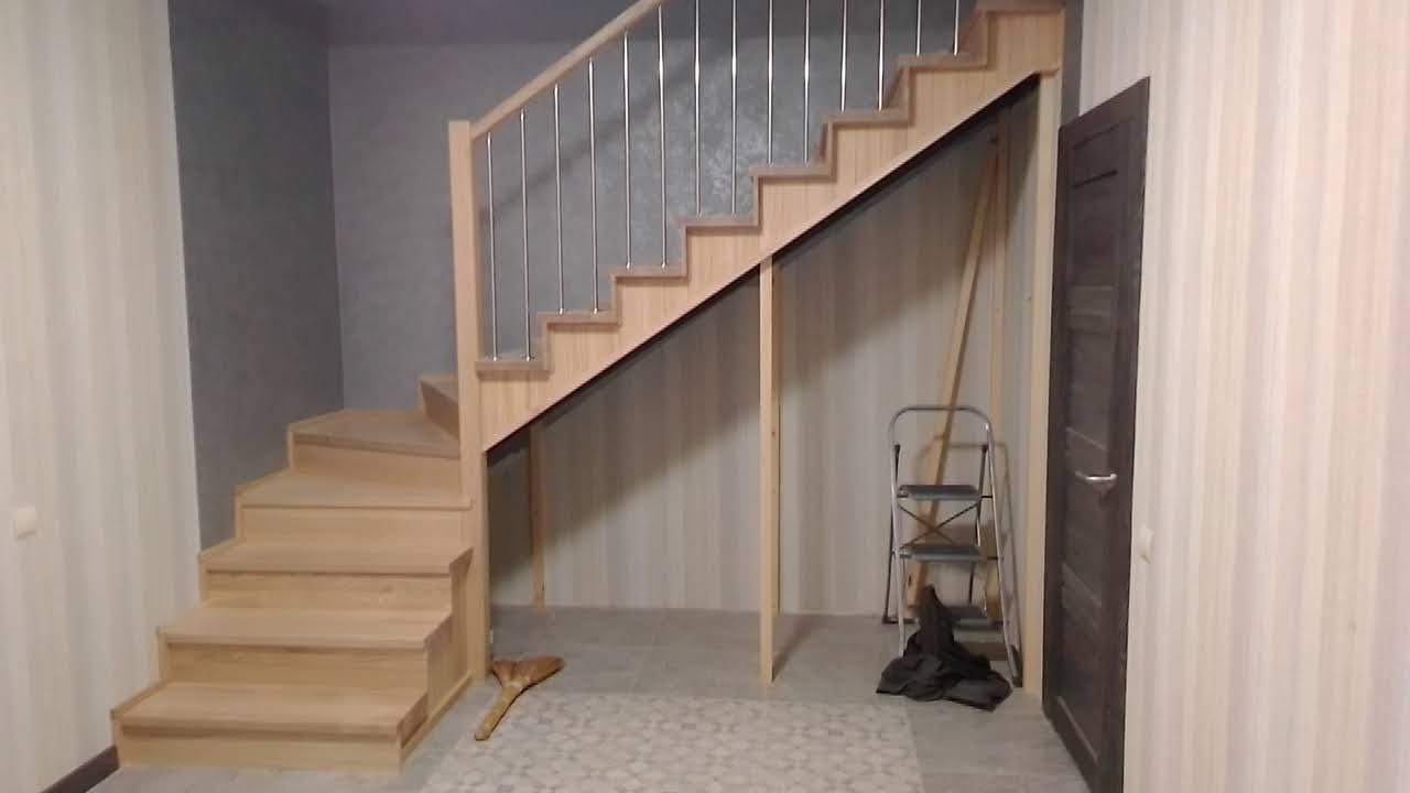 Jasne, drewniane schody z metalową balustradą w jasnym wnętrzu. Widoczna drabina oparta o ścianę i szczotka na podłodze. Ujęcie z dołu, ukazujące konstrukcję schodów.