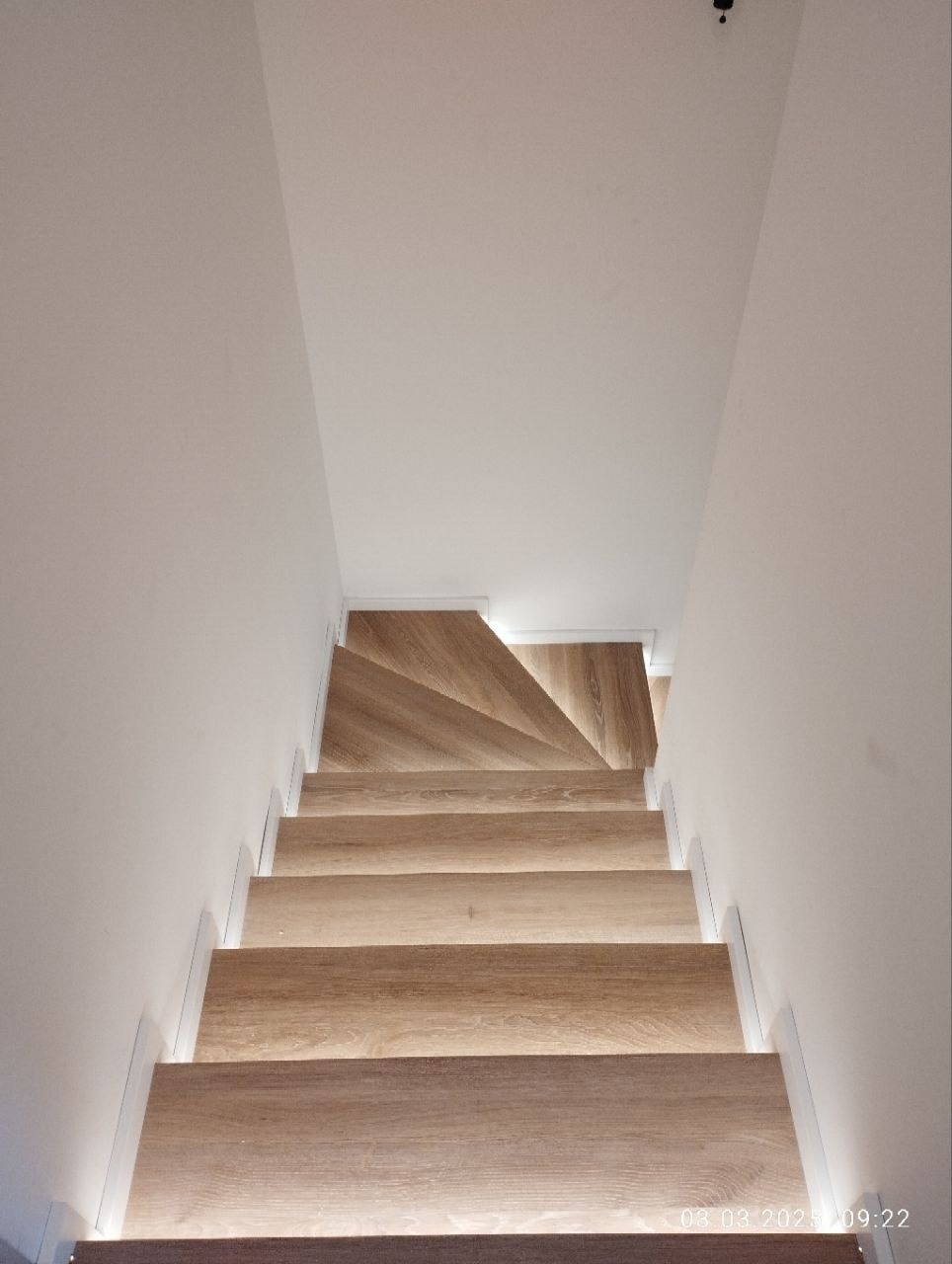 Nowoczesne schody z drewna z subtelnym podświetleniem LED, widok z góry. Jasne drewno i białe ściany tworzą minimalistyczny design.