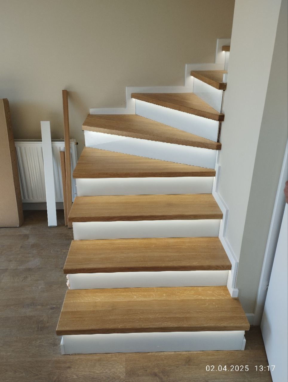 Nowoczesne schody z drewnianymi stopniami i białymi podświetlanymi podstopnicami, widok z dołu, jasne wnętrze w trakcie wykończenia.