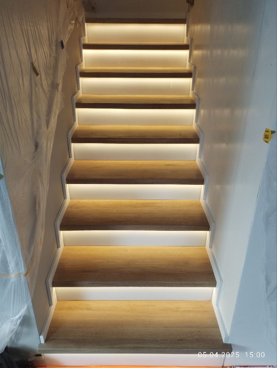 Nowoczesne schody drewniane z subtelnym oświetleniem LED, widok z dołu, podkreślający jasne, minimalistyczne wykończenie i staranne wykonanie.