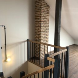 OMITEN SPÓŁKA Z OGRANICZONĄ ODPOWIEDZIALNOŚCIĄ - Klatka schodowa na poddaszu z drewnianą podłogą, ceglanym kominem i czarnymi metalowymi elementami. Oświetlenie punktowe na ścianie.