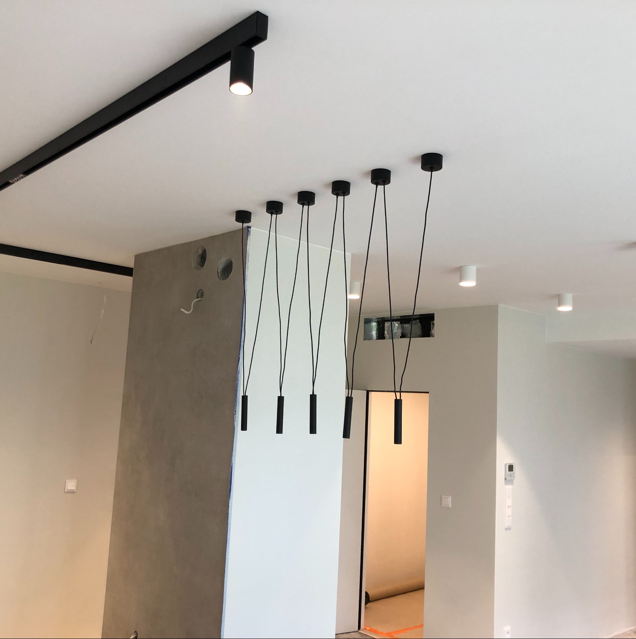 Nowoczesne oświetlenie sufitowe z czarnymi reflektorami szynowymi i wiszącymi lampami cylindrycznymi w jasnym wnętrzu z elementami szpachlowania.