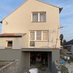 W&P TERMO-TECH - Dom po tynkowaniu z pomalowaną dolną częścią elewacji na szaro, widoczne narzędzia i materiały budowlane wokół budynku. Antena satelitarna na ścianie.