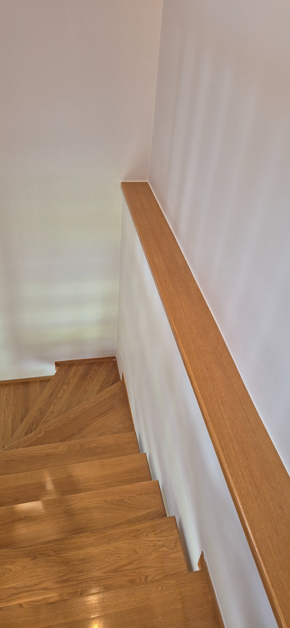 Drewniane schody z poręczą przy białej ścianie. Jasne drewno stopni i subtelne oświetlenie. Minimalistyczny design i czyste wykończenie wnętrza.