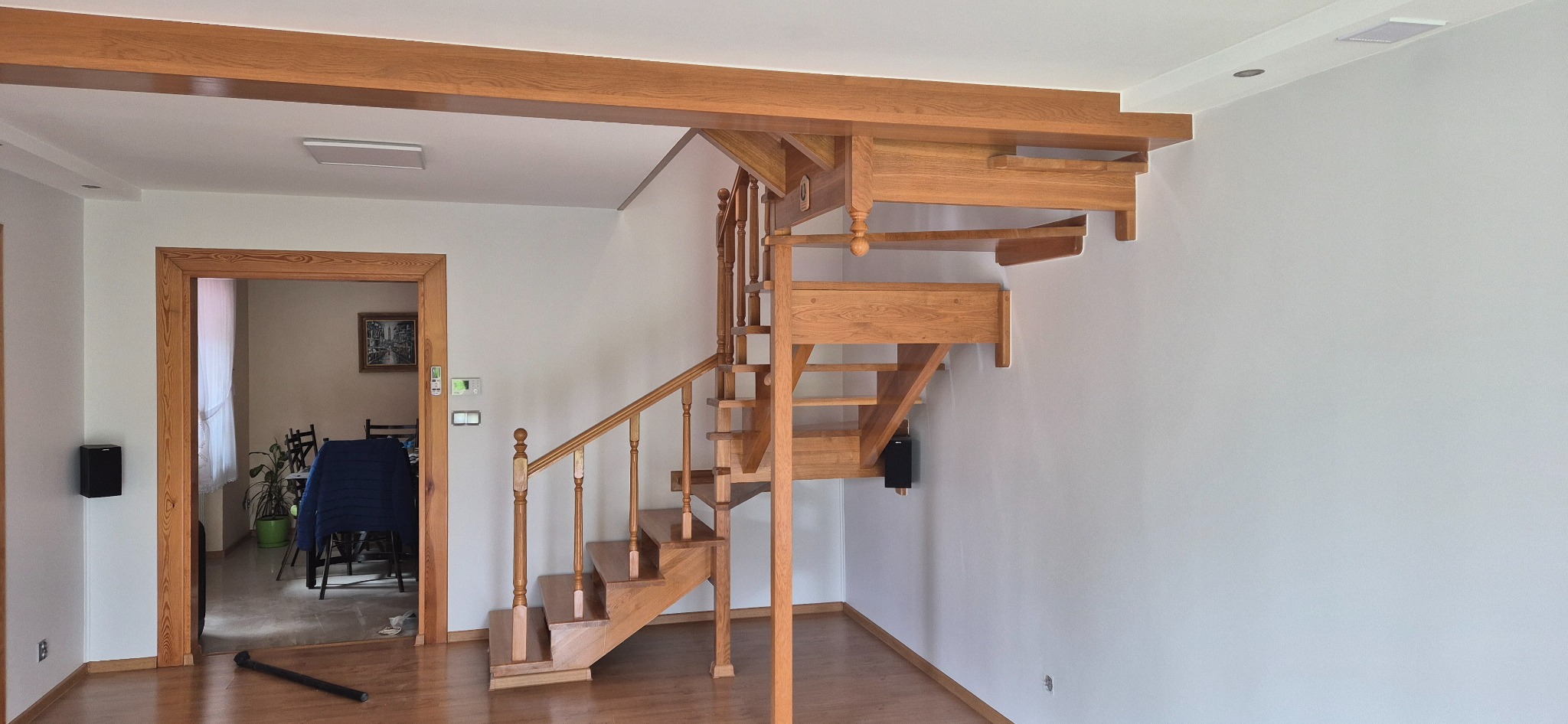 Jasne drewniane schody spiralne w nowoczesnym wnętrzu z białymi ścianami i drewnianą stolarką drzwiową. Widoczny fragment pokoju z drewnianą podłogą.