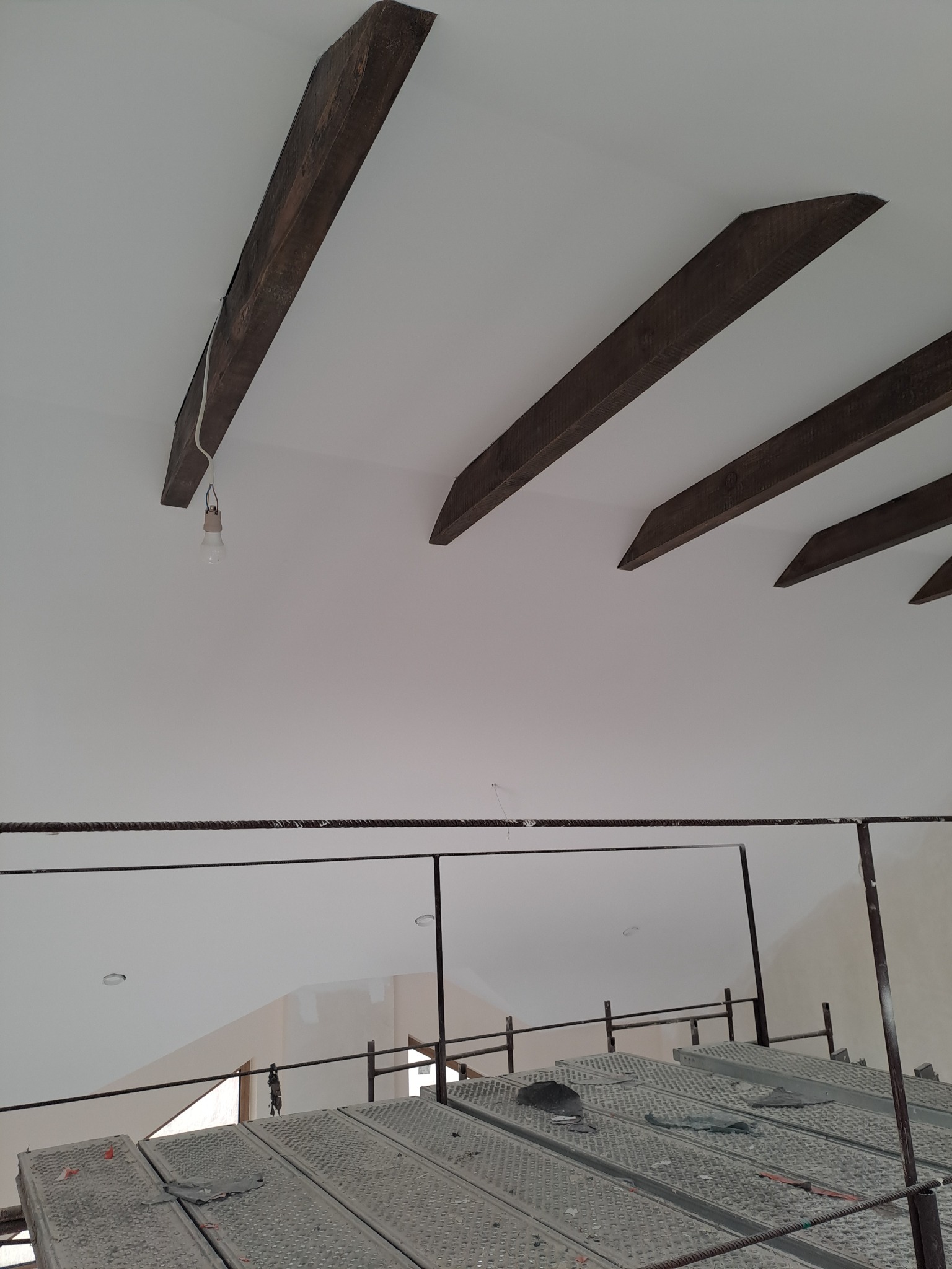 Biały sufit z drewnianymi belkami i prowizorycznym oświetleniem. Widok z rusztowania, na którym leżą szmaty. W tle ściana po szpachlowaniu.