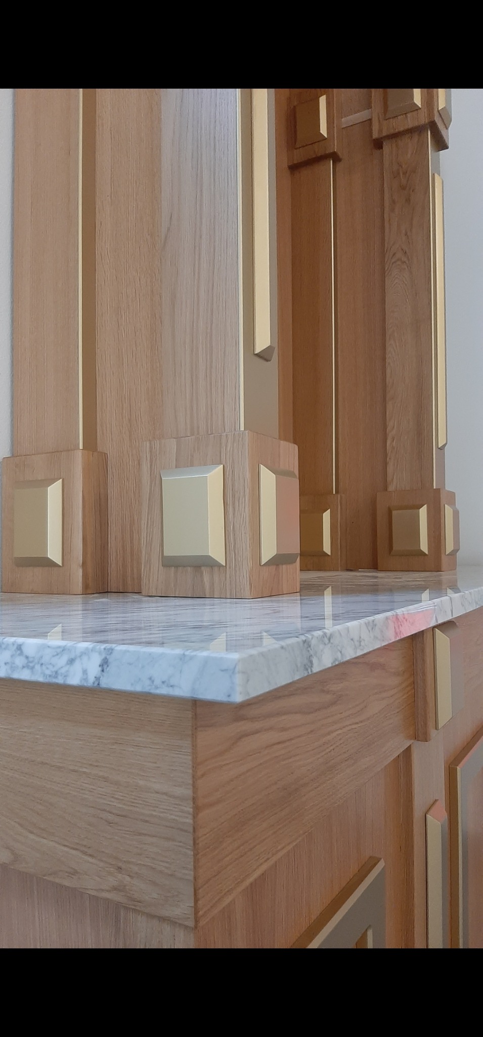 Detal drewnianej zabudowy z marmurowym blatem, złote akcenty, widoczne szafki. Starannie wykonane elementy dekoracyjne.