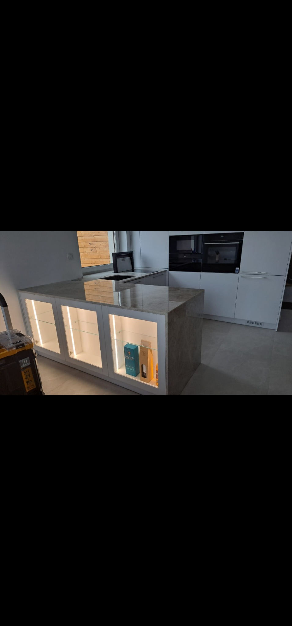 Wyspa kuchenna z marmurowym blatem i podświetlanymi szafkami, widoczna skrzynka narzędziowa, minimalistyczny design, nowoczesne oświetlenie LED.