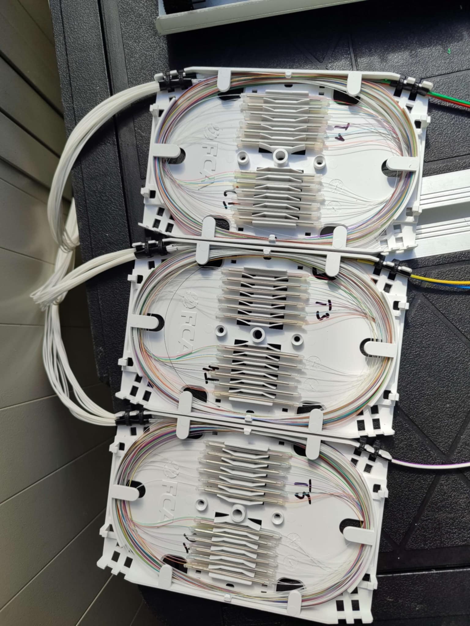 Kaskada trzech, białych kaset światłowodowych z kolorowymi włóknami, ułożonych pionowo. Kasety oznaczone numerami T1, T3 i T5. Widoczne kable światłowodowe.