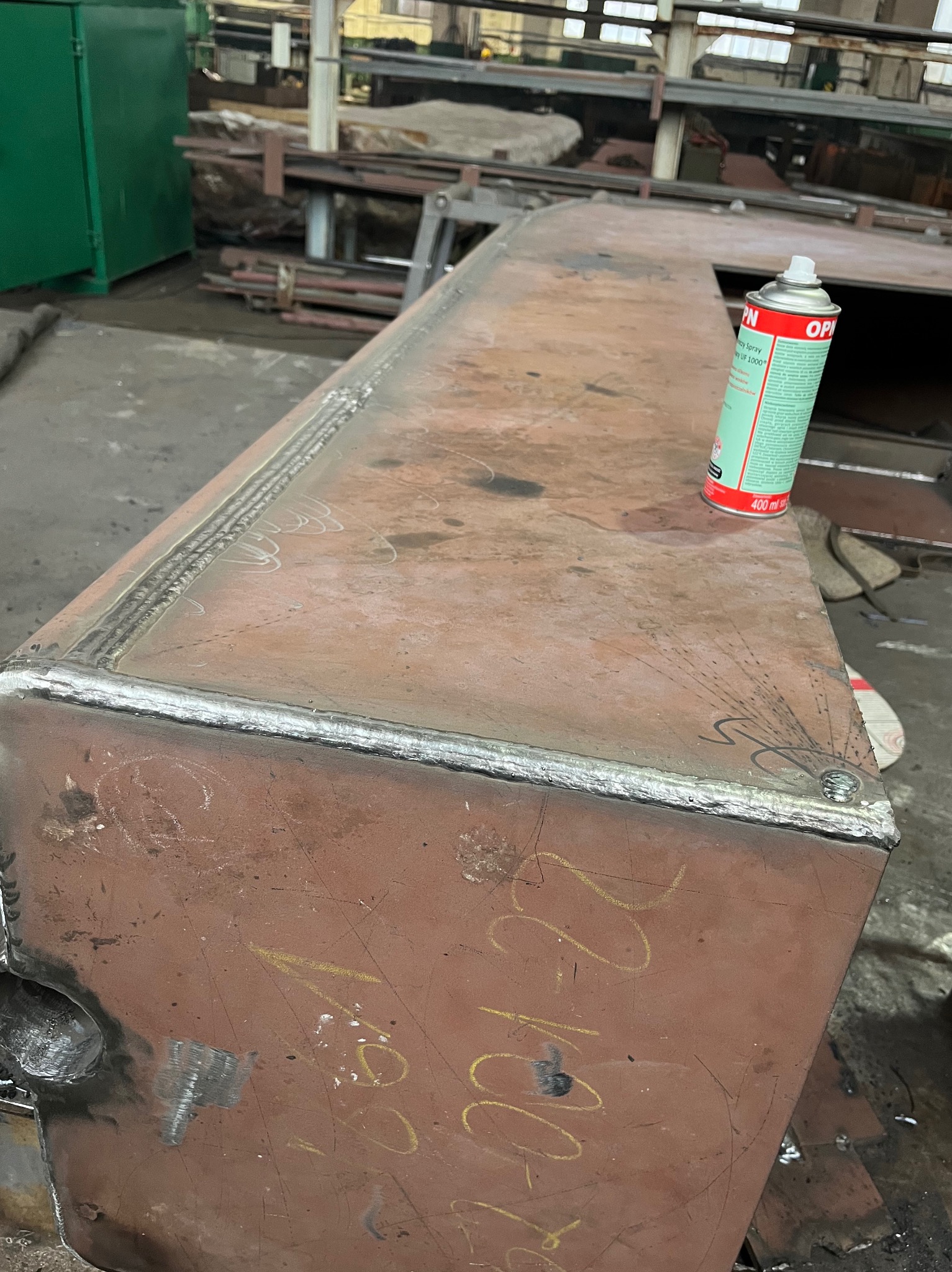 Spawana konstrukcja z blachy, widoczne spawy na krawędziach, obok puszka ze sprayem, w tle warsztat. Konstrukcja z żółtymi napisami.