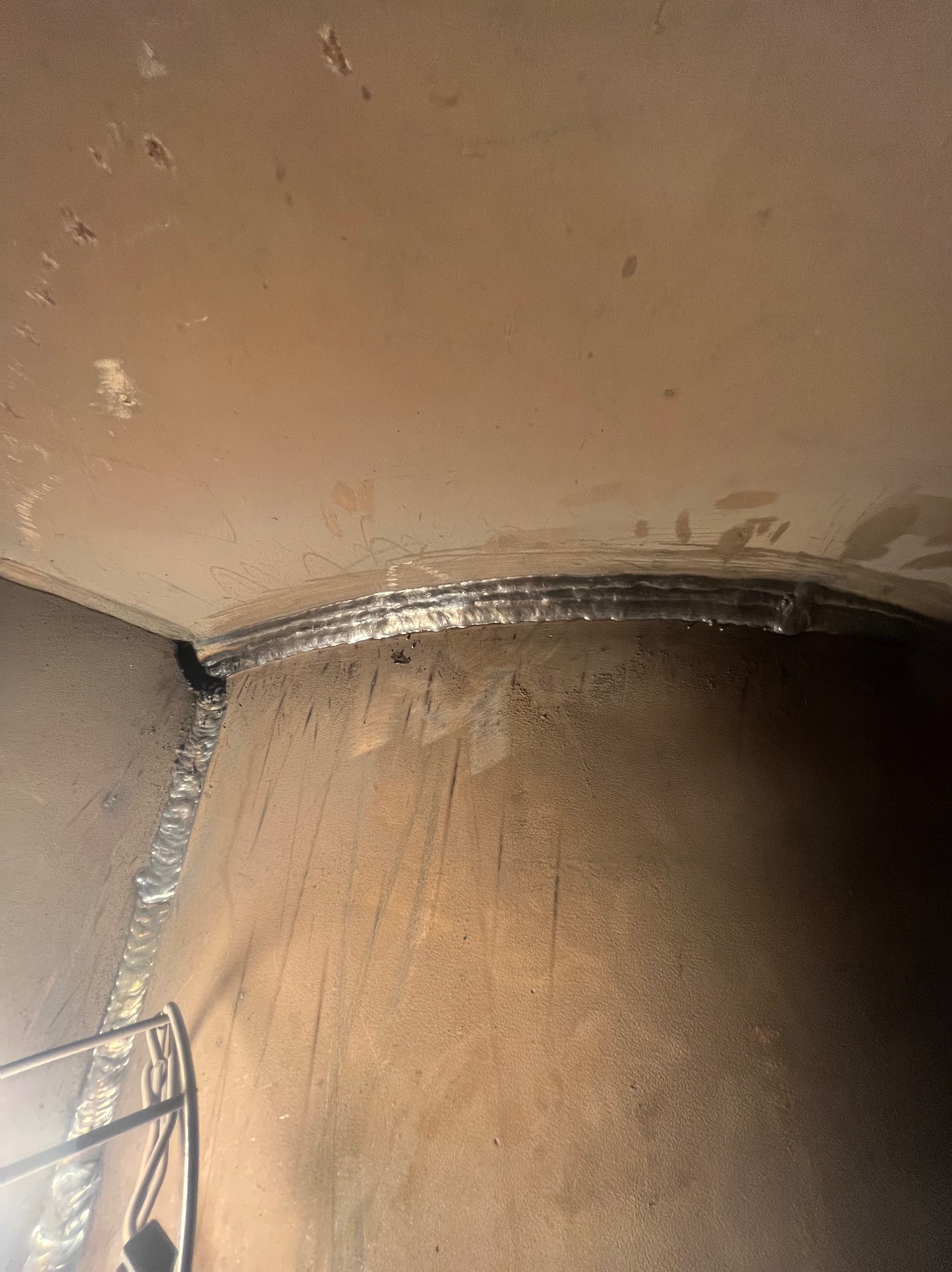 Wnętrze zbiornika po obróbce: widoczne spawy na styku ścian, metal o jednolitej barwie, ślady po obróbce. Widok z dołu, oświetlenie od góry.